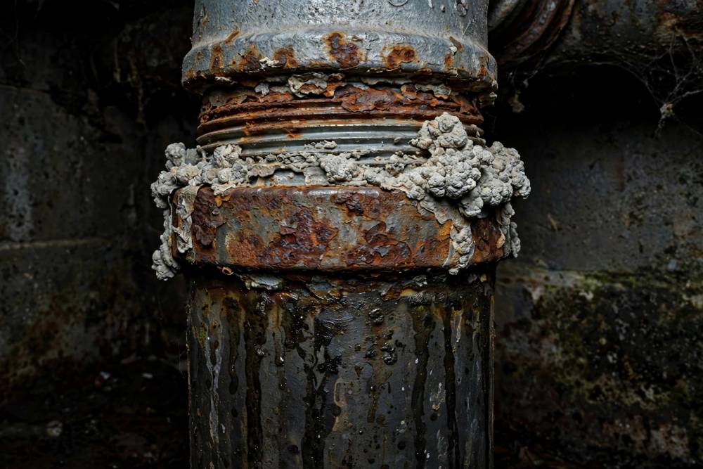 Close-up of an old galvanized steel water pipe joint with rust and mineral scale in a Red Lion basement